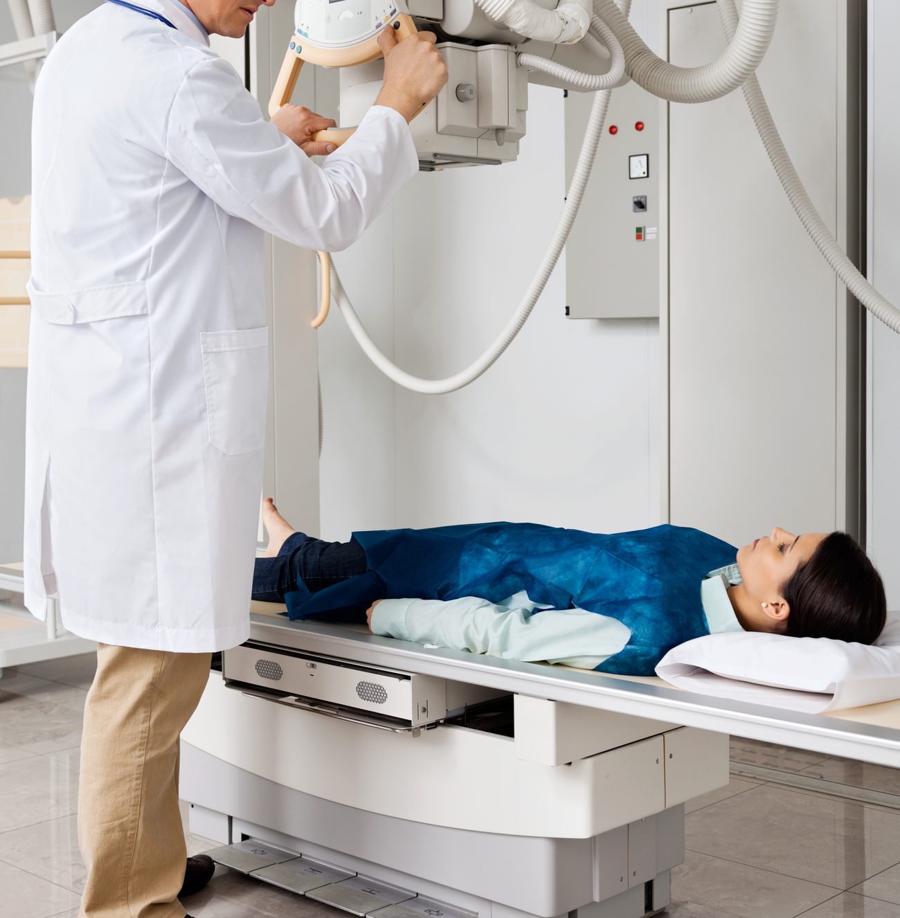 A radiographer positioning the X-ray tube above a patient lying on the table in a lead apron.